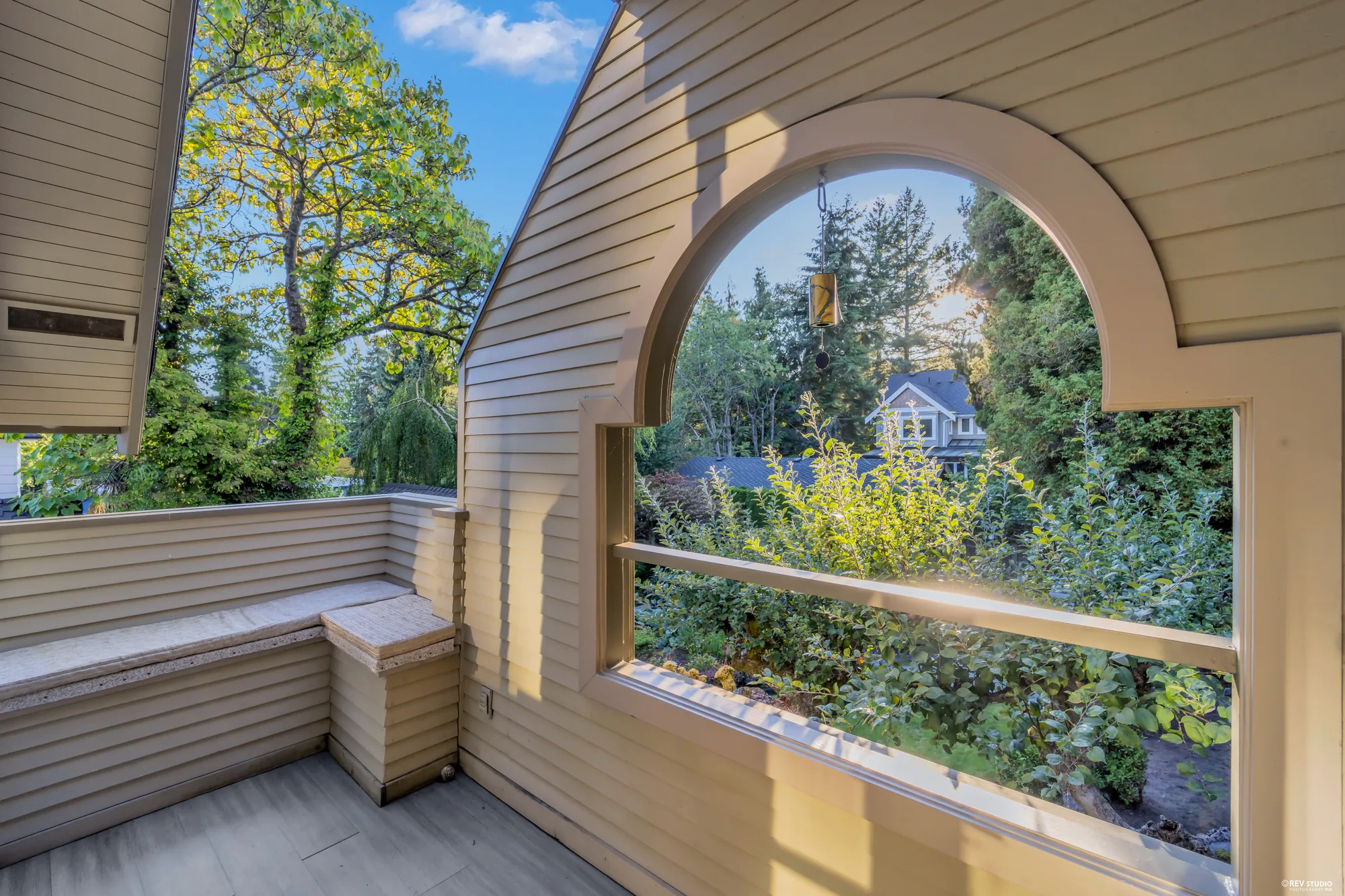 The balcony under an arched opening in the gable, a bench, the garden and the trees through the arch
