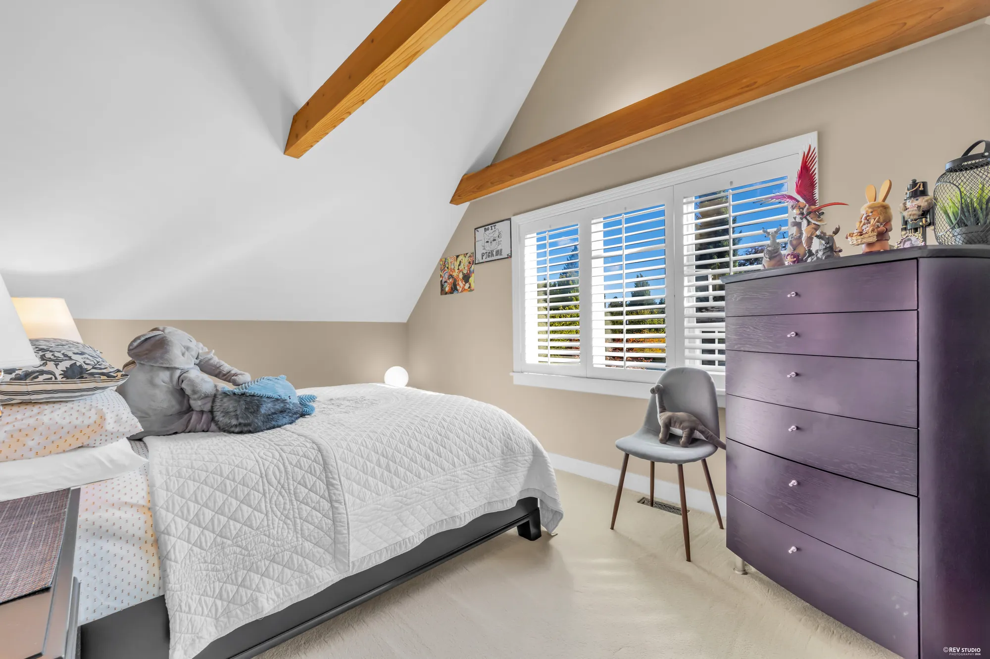 A bedroom under a vaulted ceiling with a fir beam, a shuttered window, a purple dresser