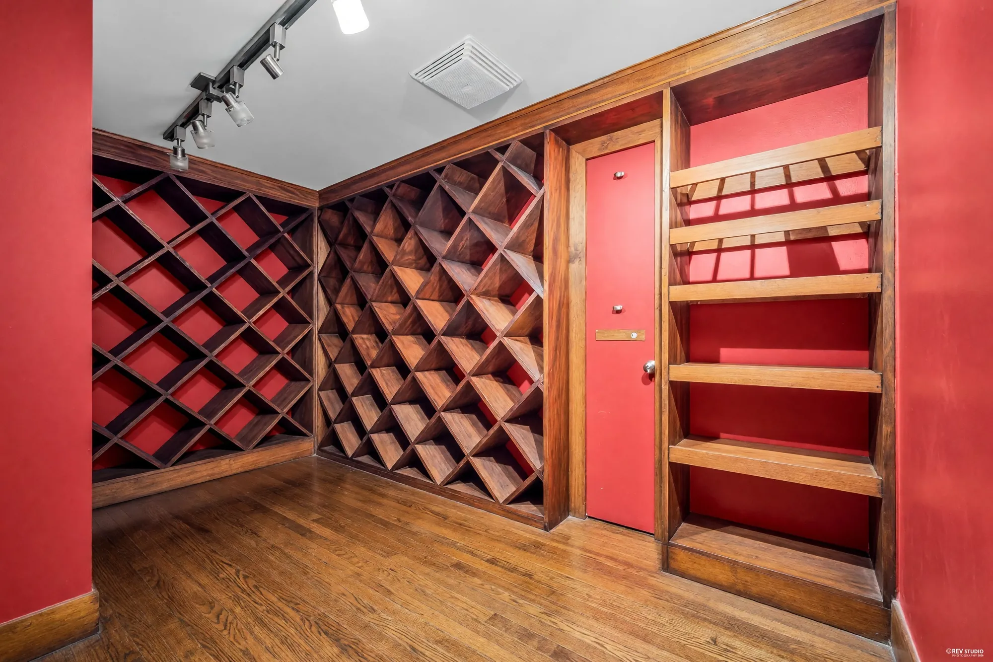 The wine cellar: red walls, diamond wine racks in wood on two walls, shelves, a red door, hardwood