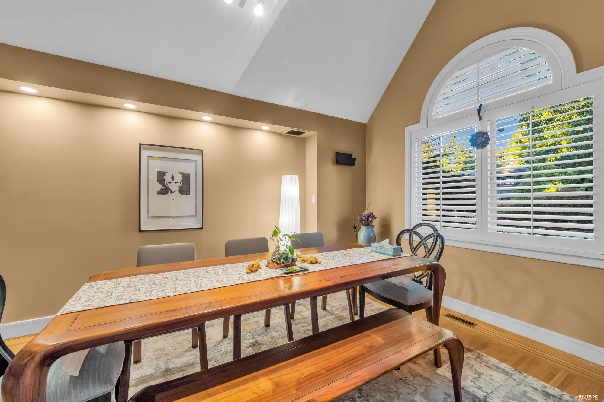 The dining table and bench toward the arched window, a print on the wall