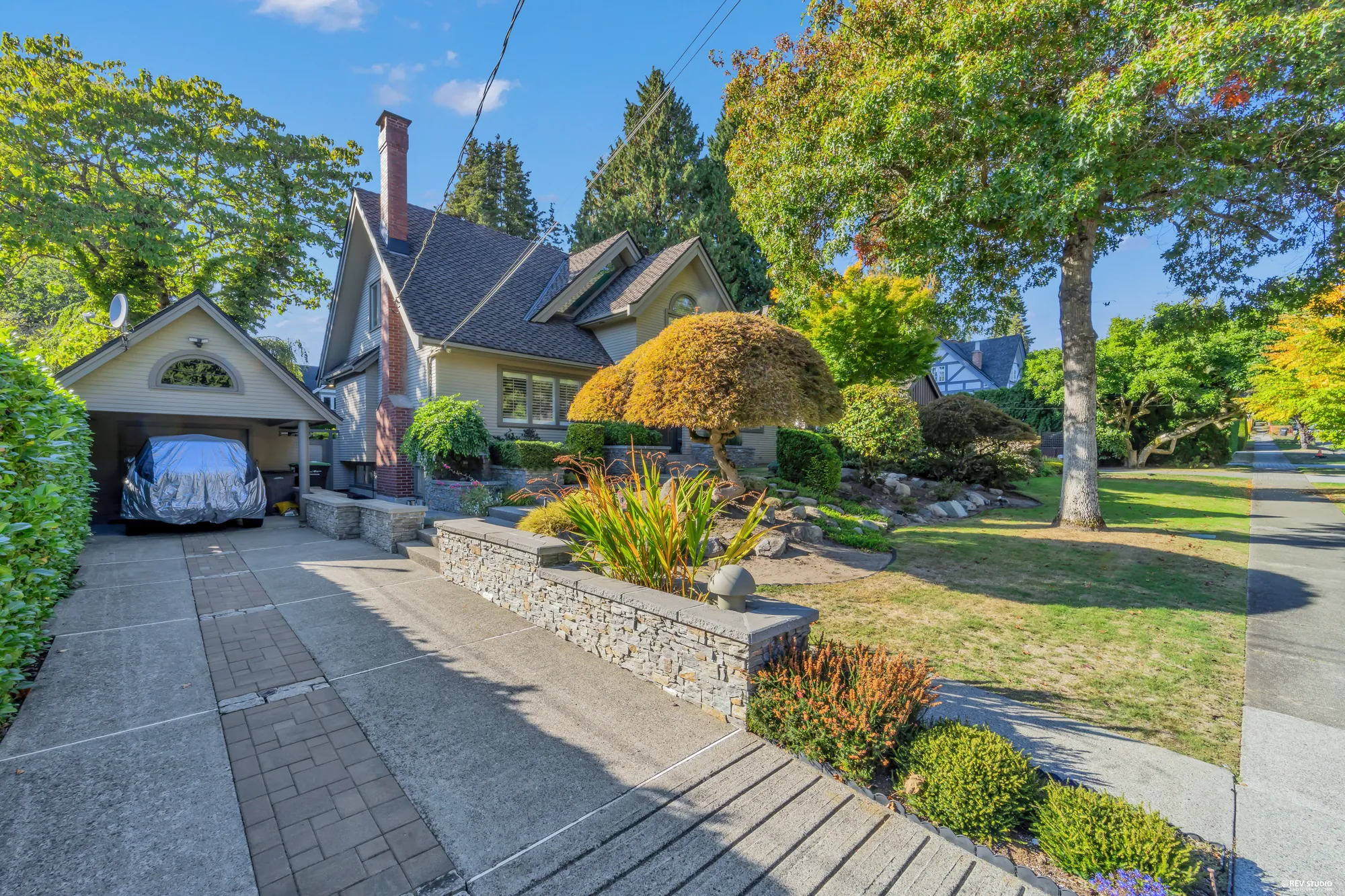 The driveway down the side of the house to the garage behind, the stone wall of the front garden on the right