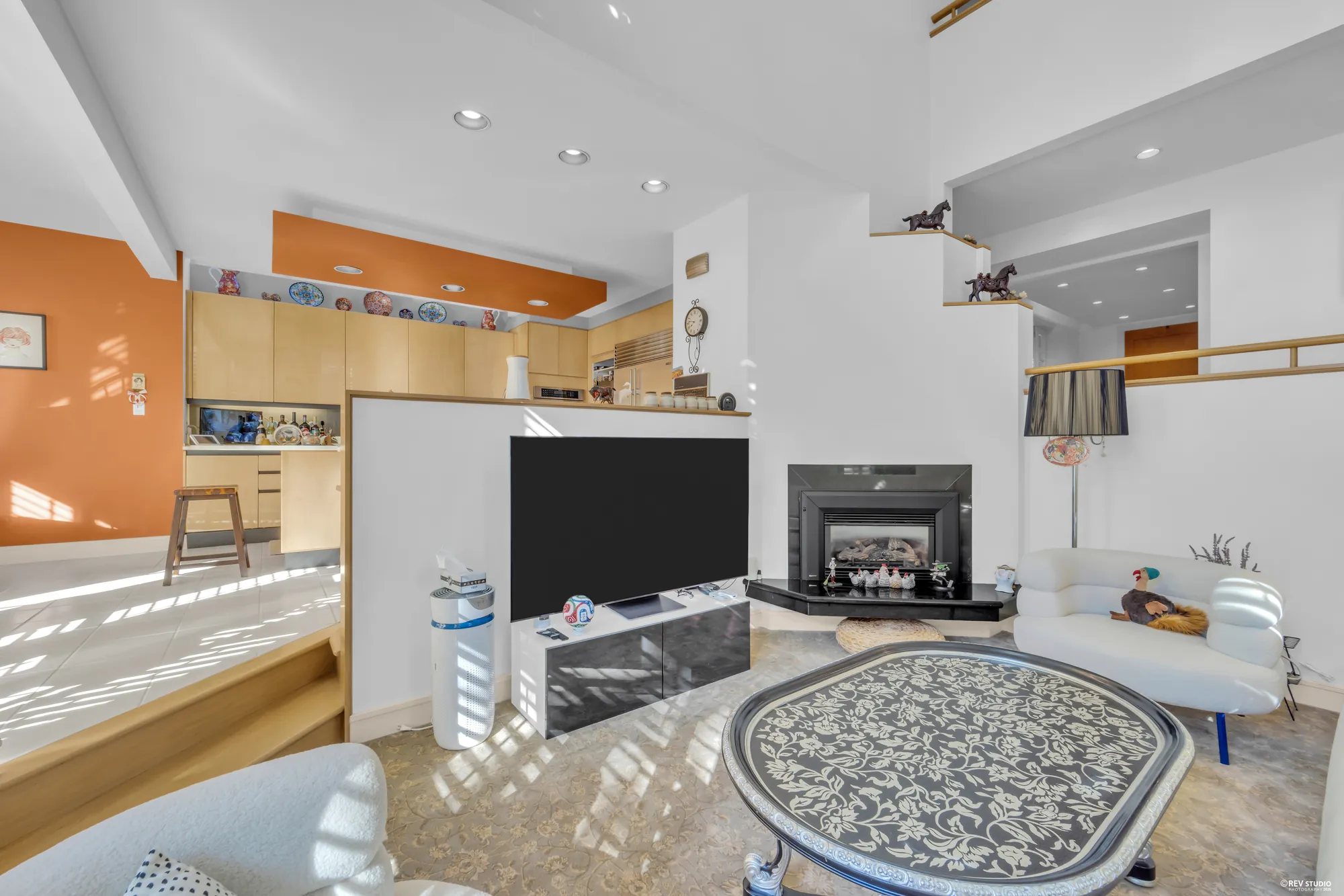 The family room from the fireplace end toward the kitchen's terracotta soffit and the stair