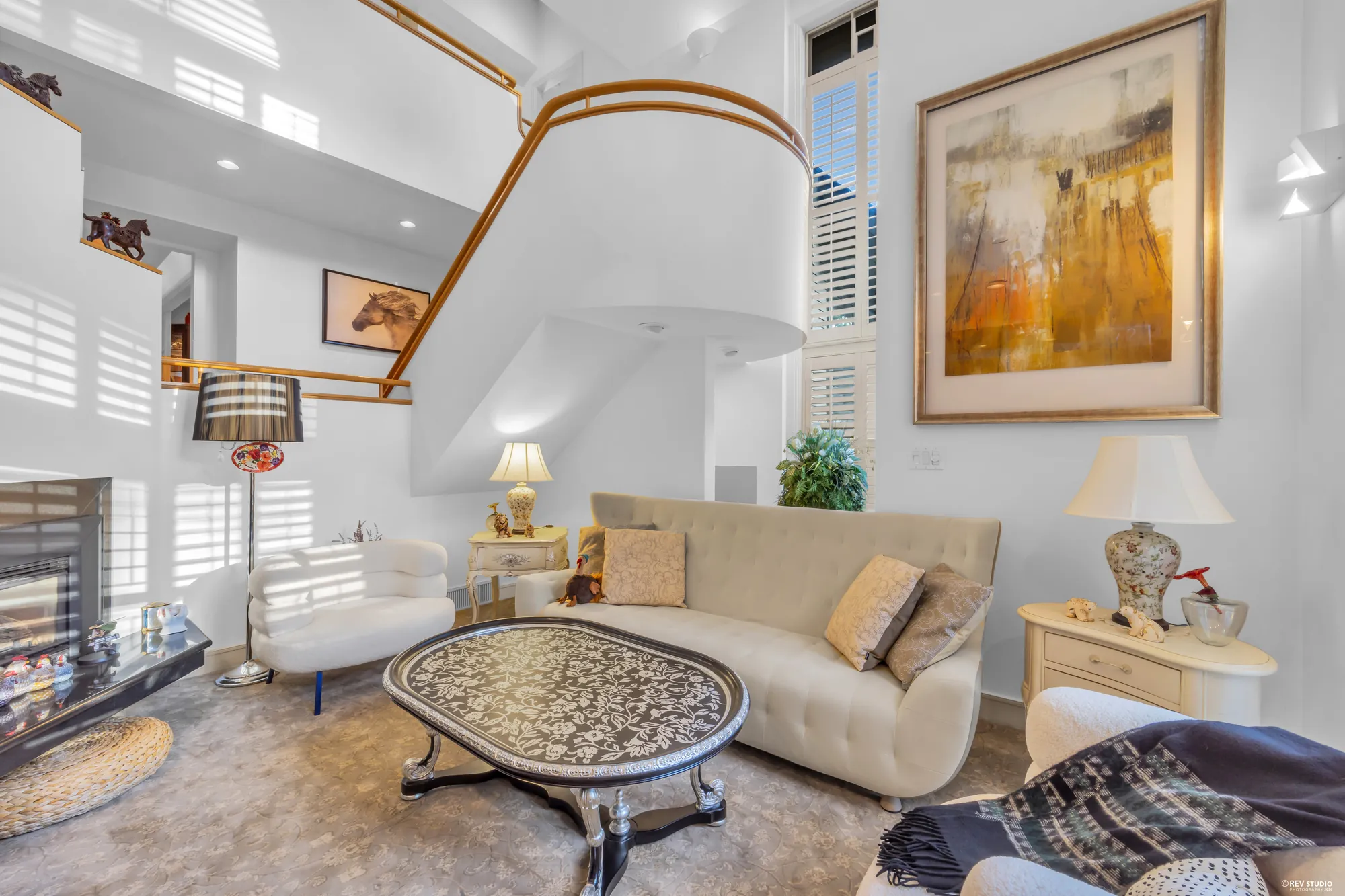The family room under the curve of the oak stair rail, a large painting on the wall, the fireplace on the left