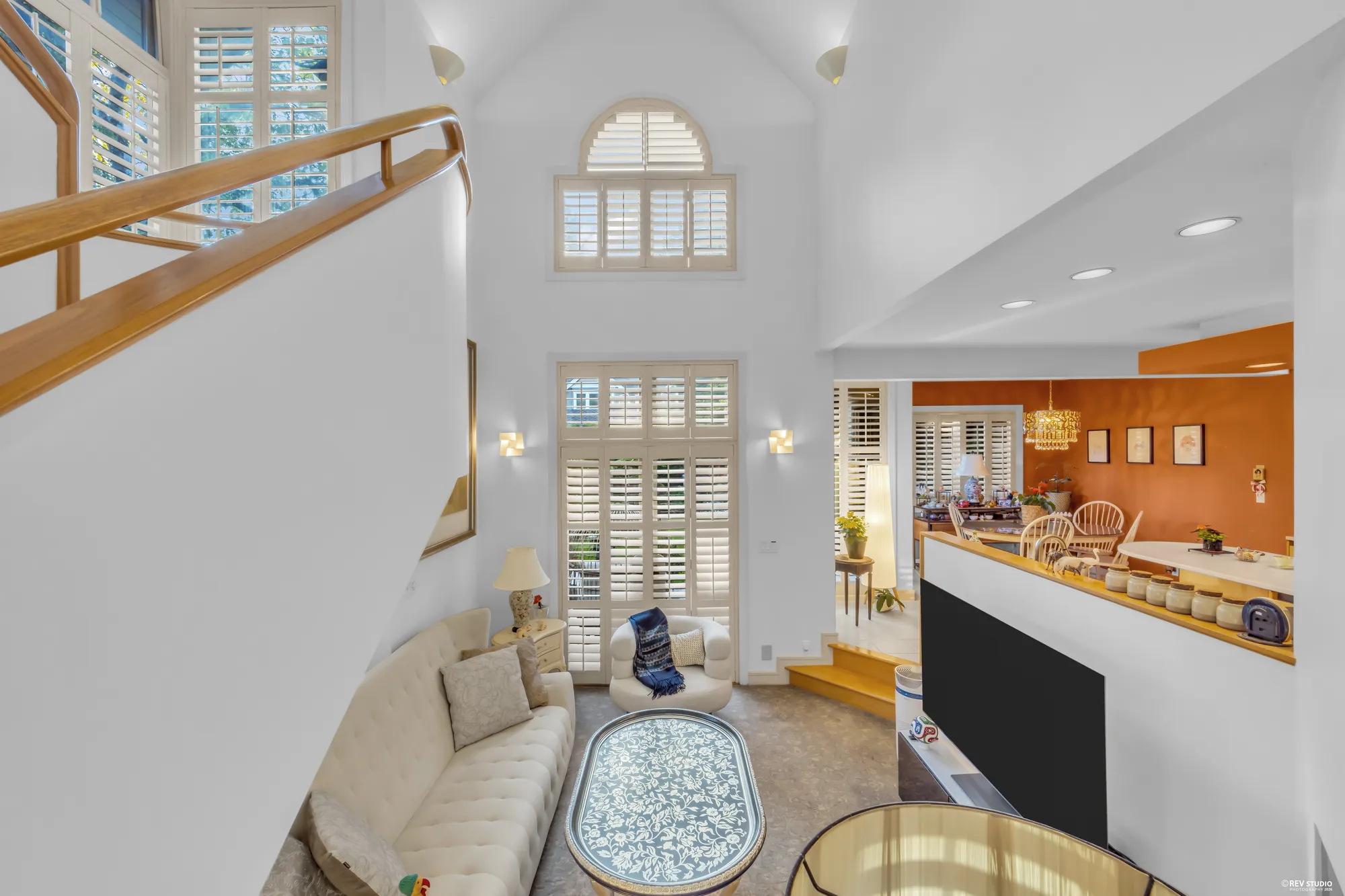 The family room from the stair: the sofas below, the kitchen's terracotta wall beyond, the tall shuttered windows