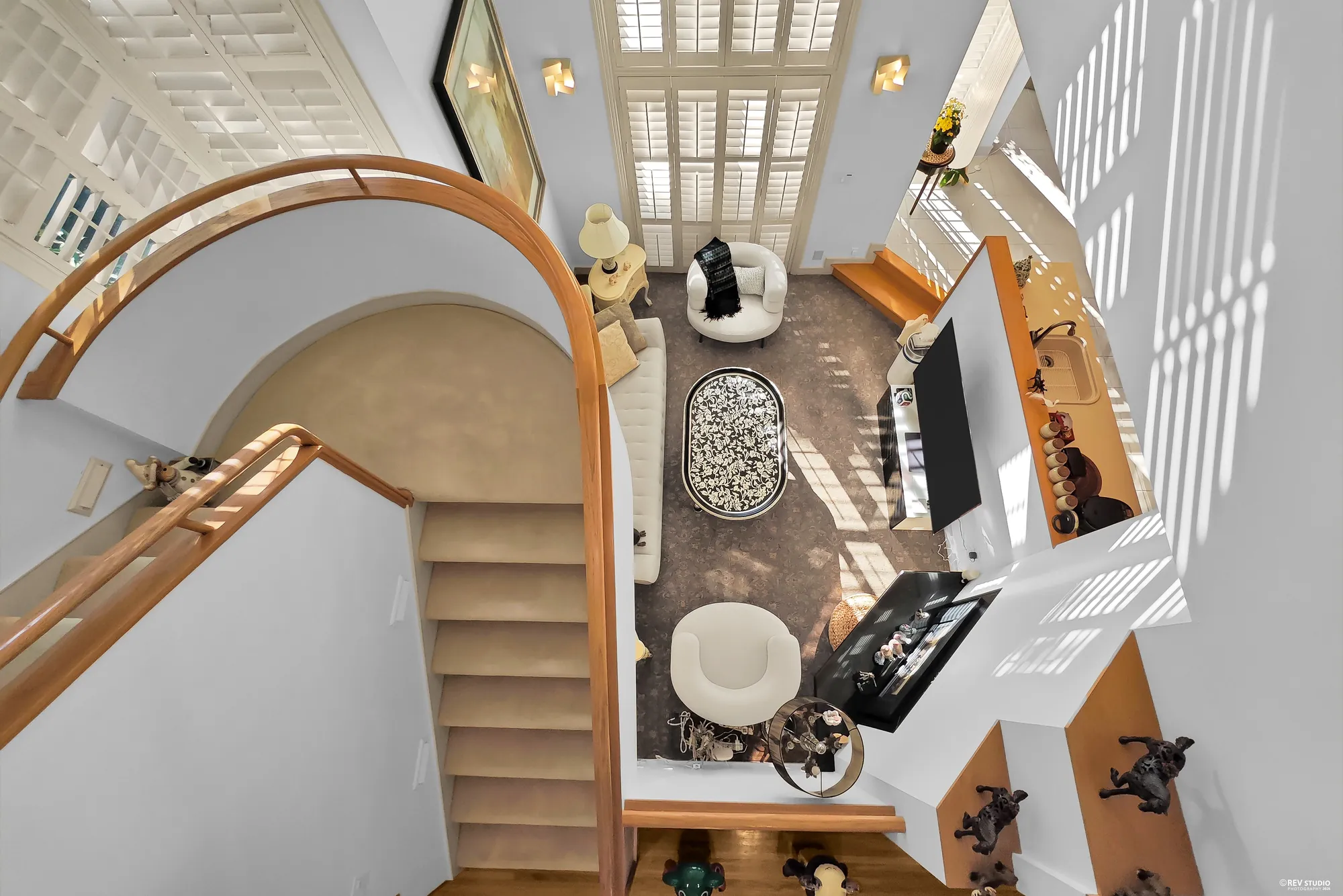 Looking straight down from the landing: the curved rail, the stair, the sofas and the brass table on the carpet below