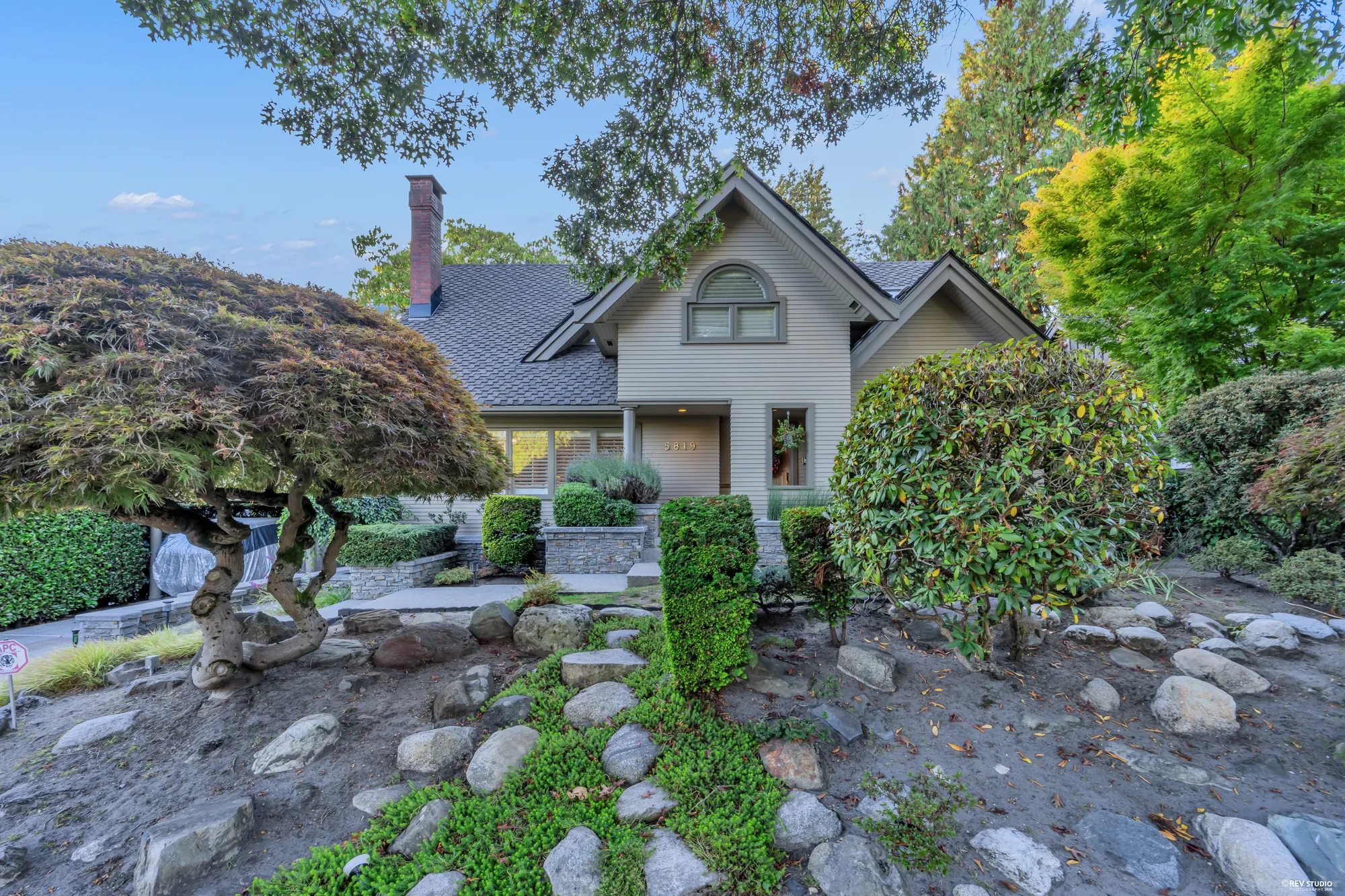 The front garden's rockery: boulders, a Japanese maple and clipped shrubs below the gables
