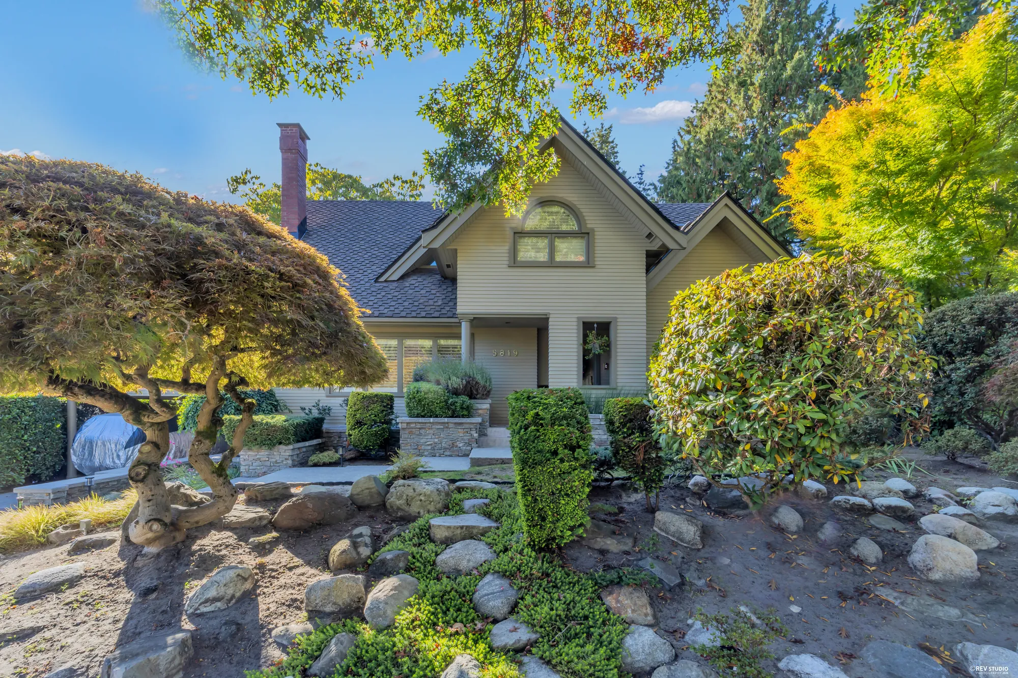 The front garden from the street corner: the maple, the boulders, the clipped shrubs and the gables