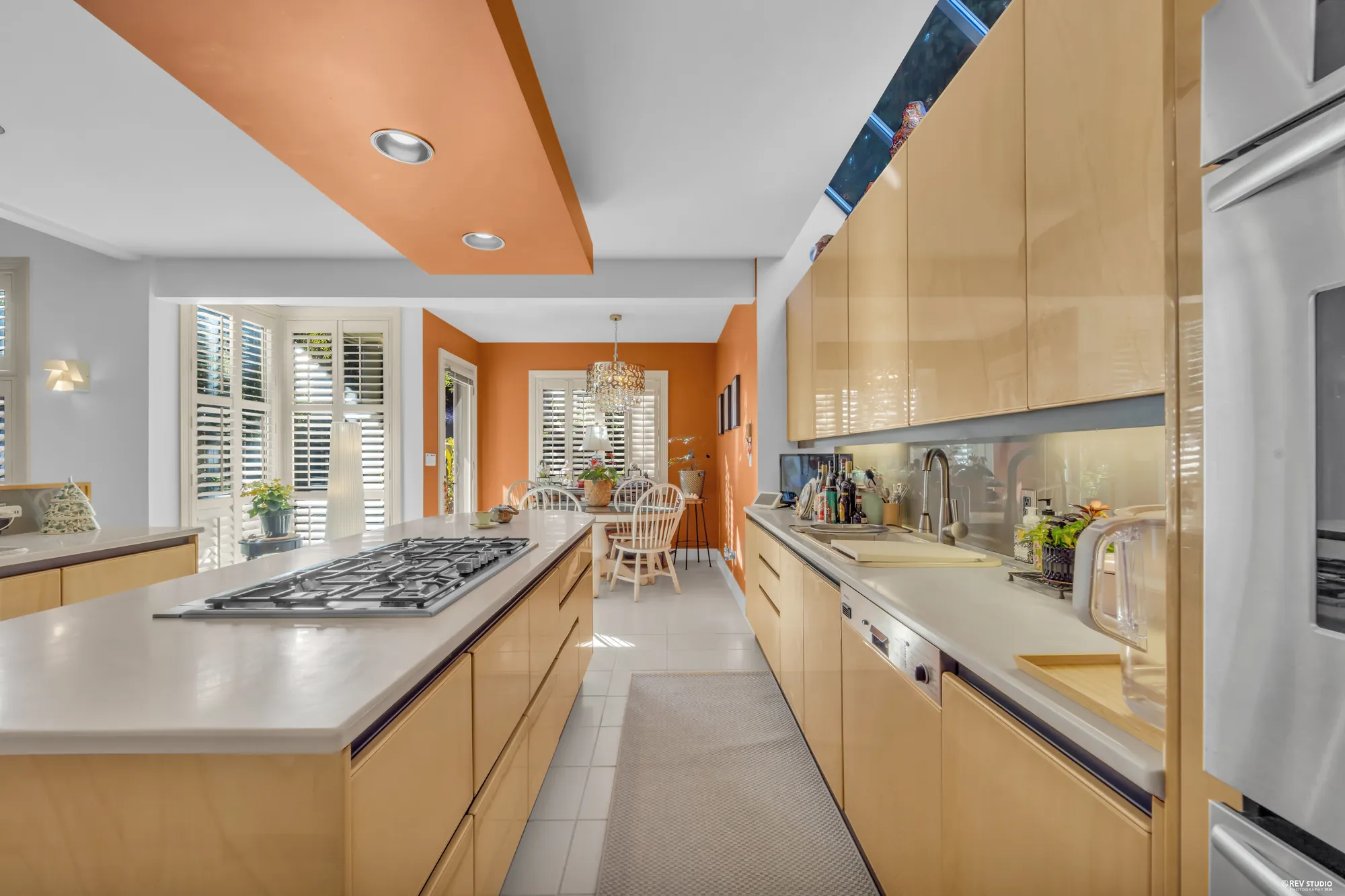 Along the island toward the nook: the cooktop, the mirrored backsplash, the chandelier of the nook beyond