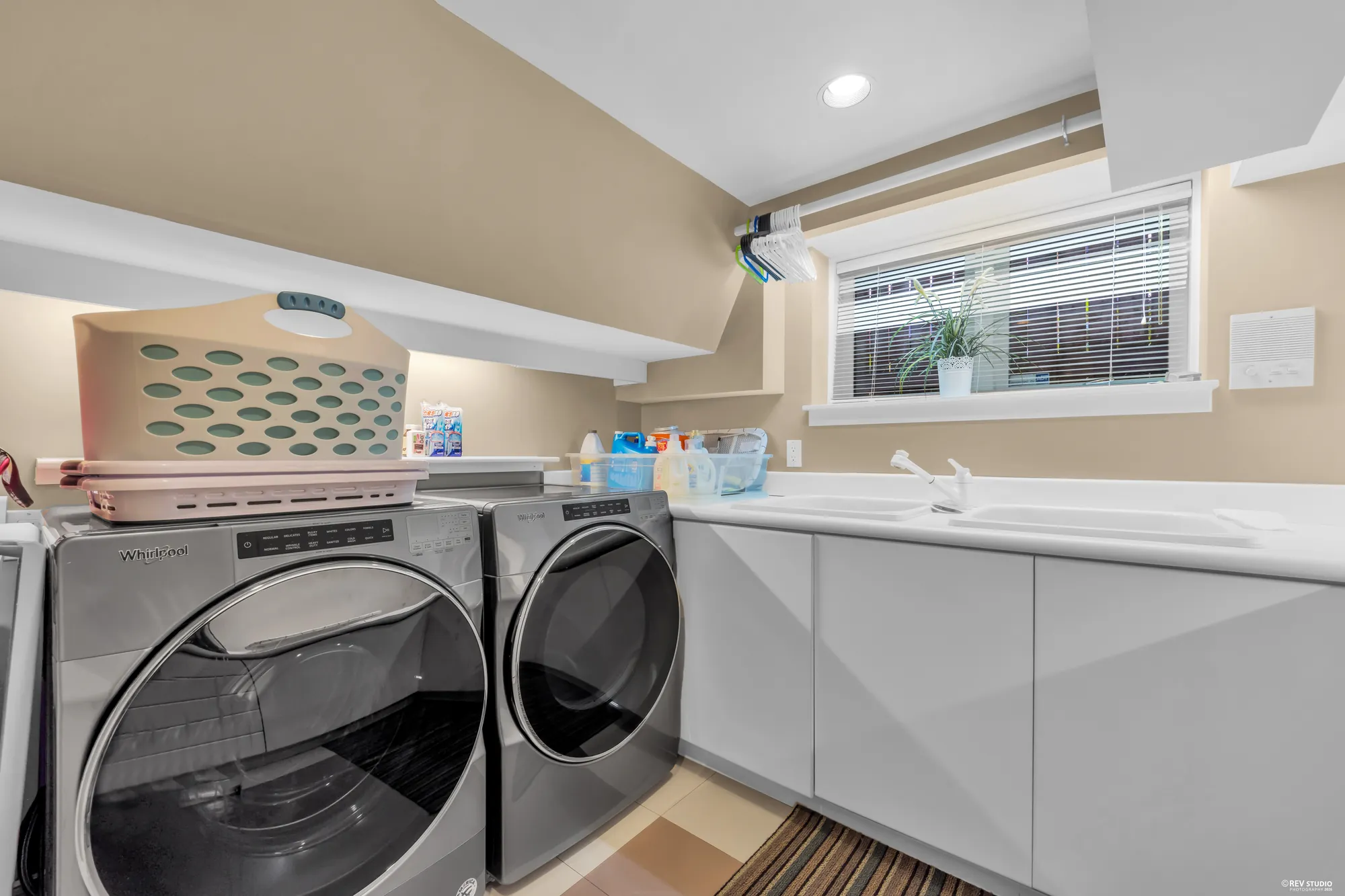 The laundry: a front-loading washer and dryer, a sink in a white counter, a window
