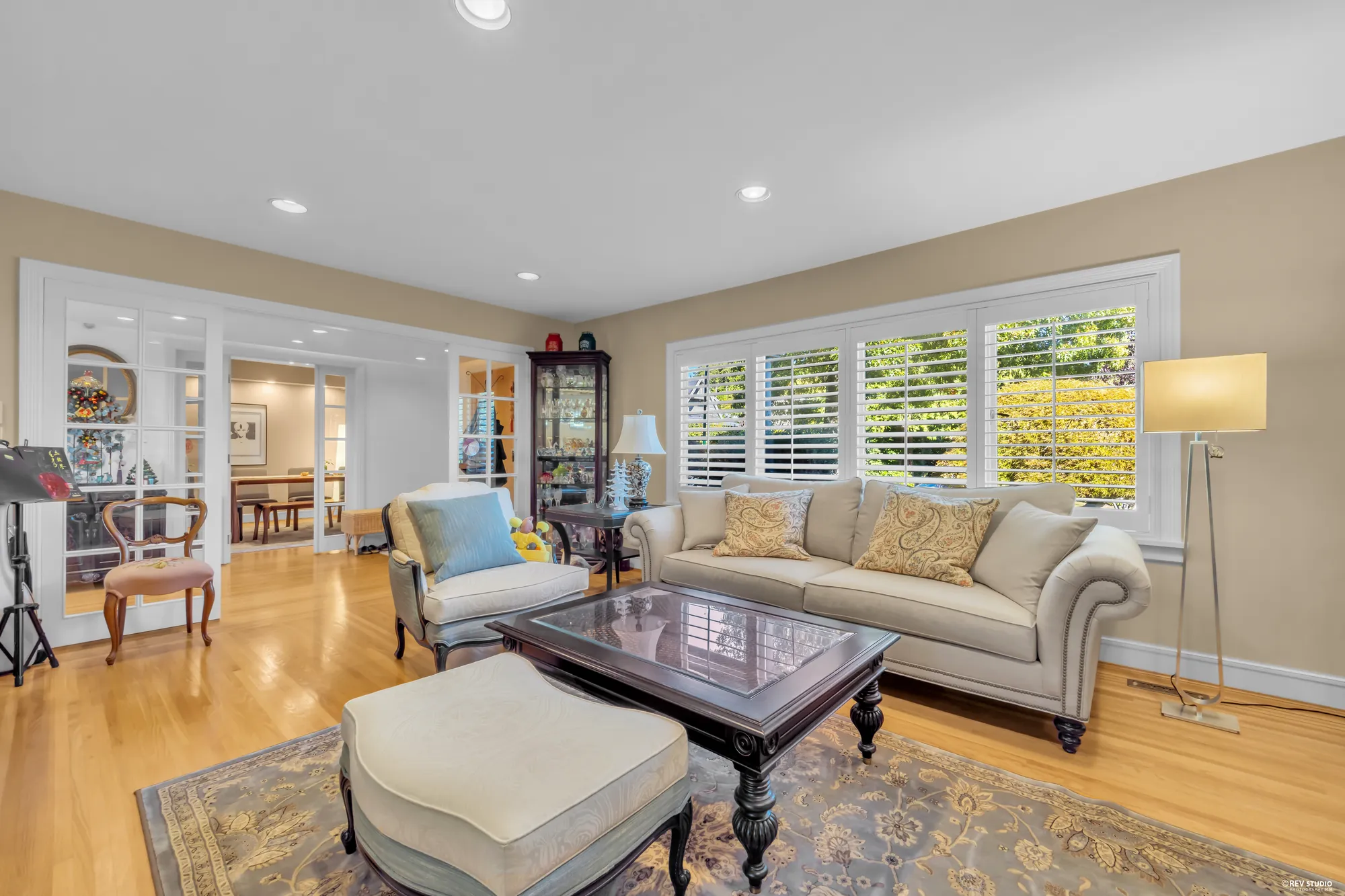 The living room: cream sofas on hardwood, a wide window with plantation shutters, French doors to the foyer on the left