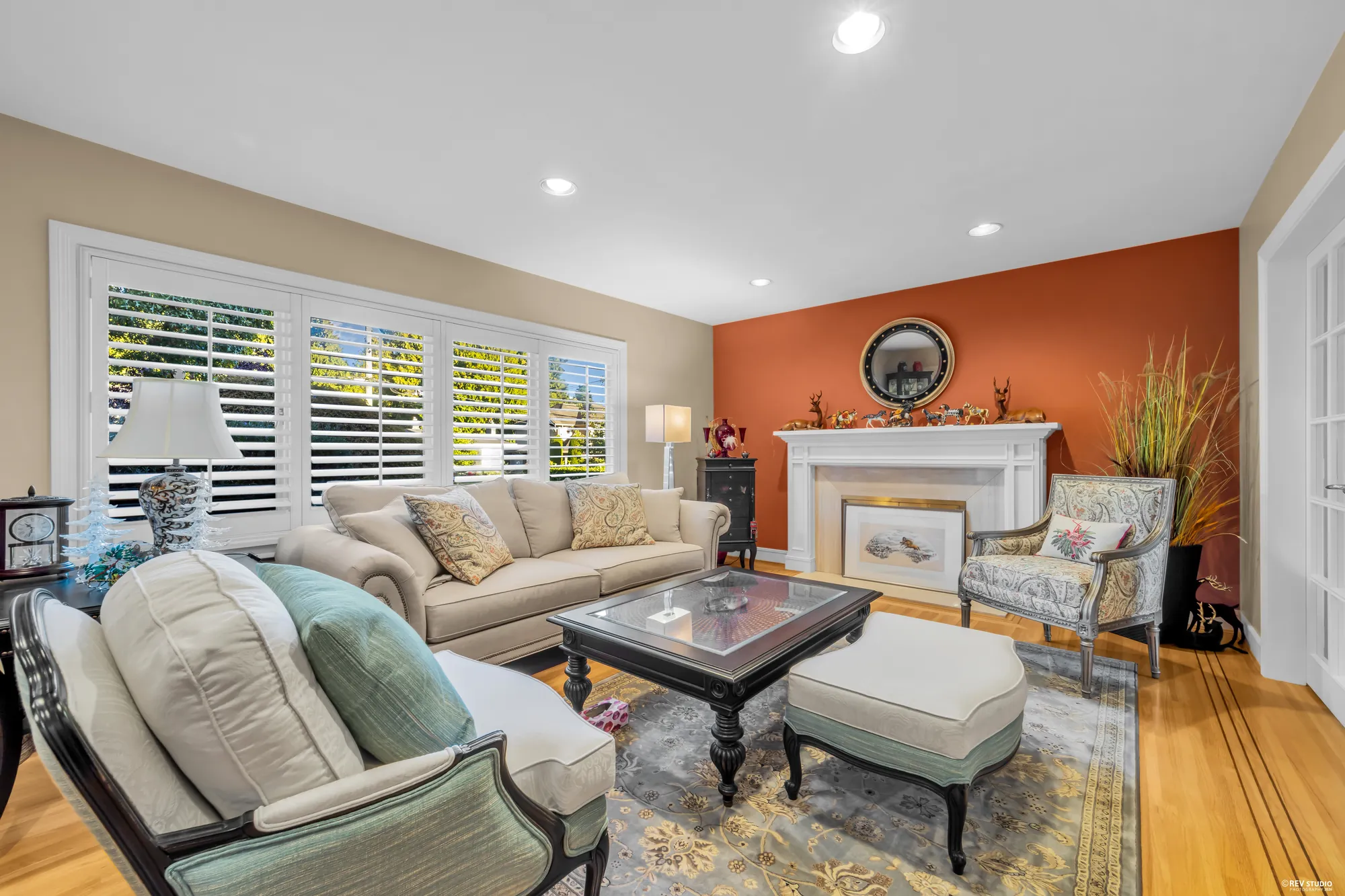 The living room's fireplace with a white mantel on a terracotta wall, armchairs either side, the shuttered window on the left