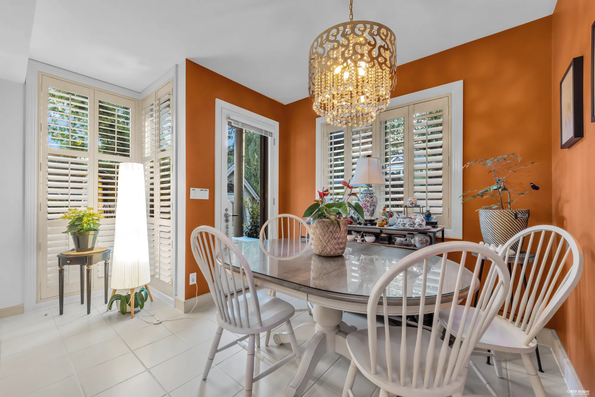 The breakfast nook: a round table and chairs under a chandelier, a terracotta wall, shutters and a door to the patio