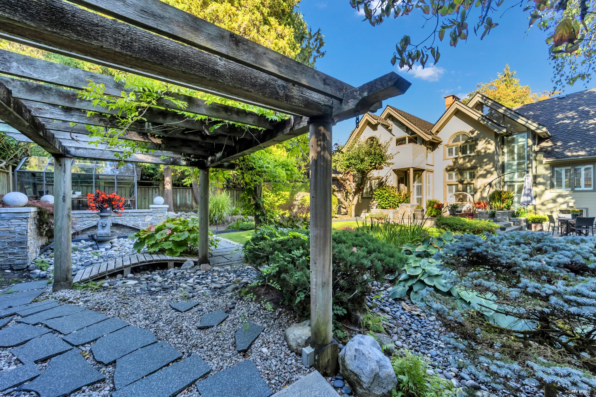 From the pergola toward the house: the stone path, the pond, the gables beyond