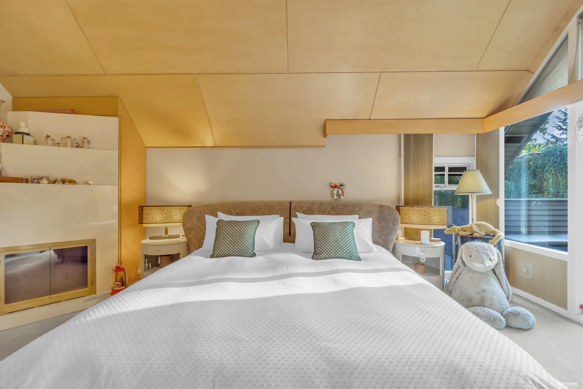 The primary bedroom: a bed under a vaulted wood ceiling, sliding glass doors to the balcony and the trees beyond