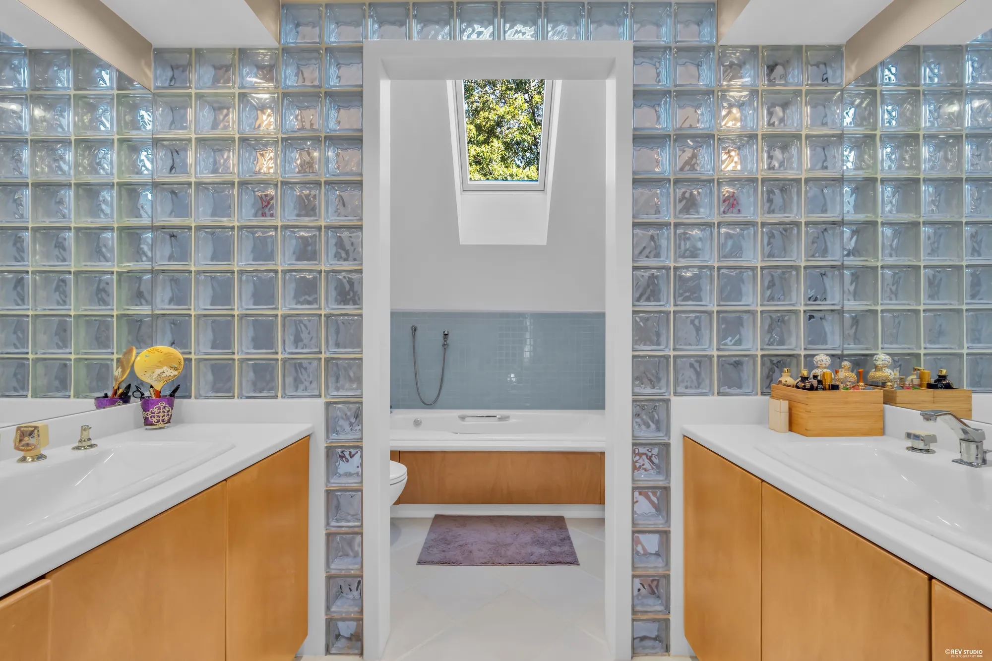 The primary bathroom: a vanity either side of a glass-block passage to the tub, a skylight over the tub